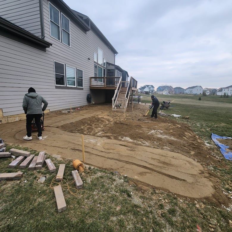 Crew compacting the sand and gravel base for a new backyard paver patio.